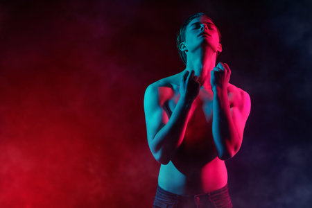 Portrait of a handsome athletic young man posing with naked torso in red and blue light. Man's...