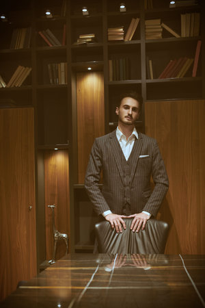 Handsome brunet man in an elegant suit poses in a luxury apartment. Mafia. Male beauty, fashion.