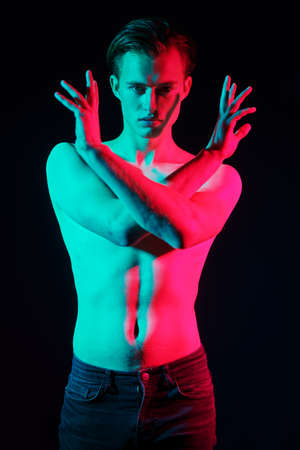 Art portrait of a handsome athletic young man posing with naked torso in red and green light. Man's beauty and health. Art portrait.の写真素材
