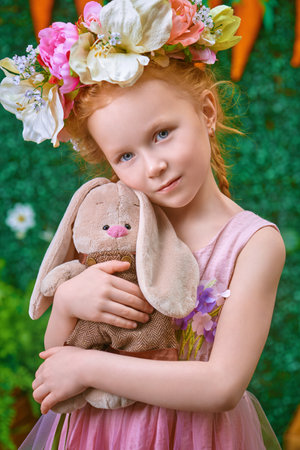 Portrait of a cute red-haired girl in a wreath of flowers embracing her toy bunny Beauty. Easter holiday. Childhood. Spring-summer season.の写真素材