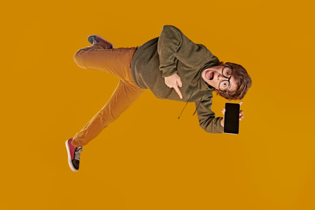 Emotional teen boy is flying through the air, screaming holding in his hands the phone. Yellow...