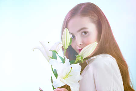 Beautiful young tender girl with lily flowers in a light pink-blue haze. Inspiration of spring and summer. Perfume, cosmetics concept.の写真素材