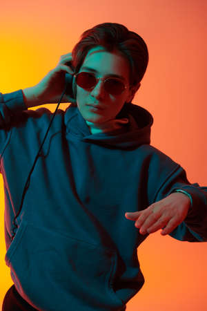 Emotional boy teenager listens to music with headphones and enjoys. Youth culture. Studio portrait in mixed color light.の写真素材