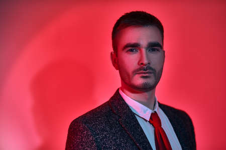 Modern stylish man in elegant suit posing in red and crimson lighting. Men's fashion.の写真素材