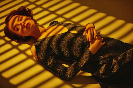 Beautiful girl in evening dress lies on the floor in the shade of sunset. Hair and makeup in the style of the 20s. Art fashion.の写真素材