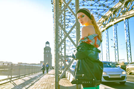 Trendy girl with bright makeup poses in stylish colorful clothes on a bridge in a big city. Fashionable urban style.の写真素材