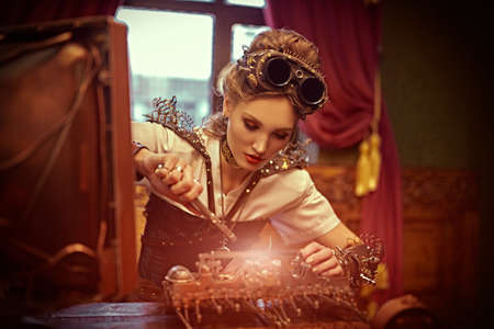 Beautiful steampunk lady scientist inventor repairs the mechanism in her laboratory with Victorian interior.の写真素材