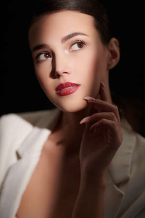 Close-up portrait of dramy beautiful brunette woman poses in elegant black lace blouse on a black background. Studio portrait with light and shadows. Makeup and cosmetics.の写真素材