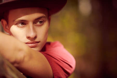 Close-up portrait of a handsome young man looking away in hat in light and shadow. Male beauty.の写真素材