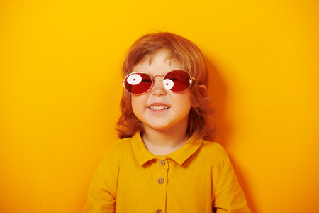 Portrait of a happy little girl having fun with sunglasses. Bright yellow background. Child,...
