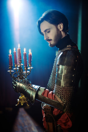 Portrait of a medieval knight in armor standing with candles in the castle.の写真素材