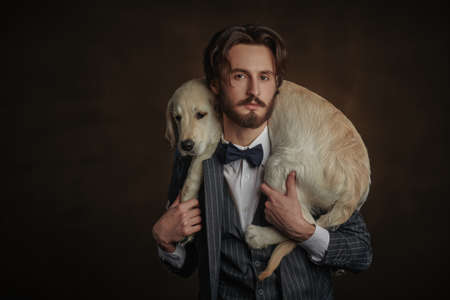 Fashion, man and dog. Portrait of a handsome man in elegant suit holding his Golden Retriever dog on a black background.の写真素材