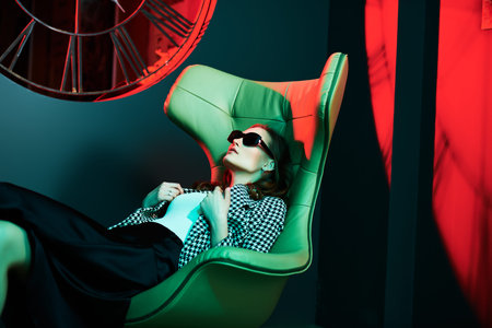 Fashionable lady in stylish clothes and sunglasses poses on a leather armchair in a luxury apartment. Fashion shot.の写真素材