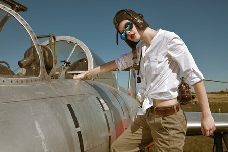 Portrait of a beautiful girl pilot wearing helmet and sunglasses stands next to her fighter jet at...