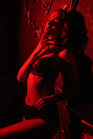 Seductive young woman poses in black sexy lingerie in a vintage interior in red light. Underwear fashion.の写真素材