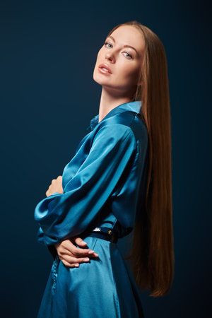 Fashion shot. Beautiful fashion model girl with long straight hair poses in blue satin dress on a dark blue background.の写真素材