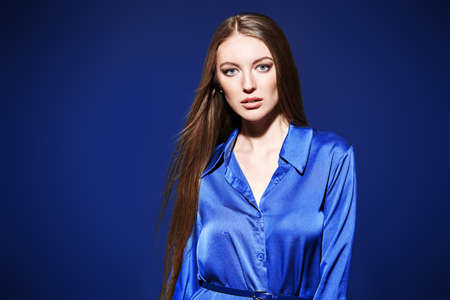 Fashion model girl with beautiful long hair poses in evening satin dress in motion. Studio portrait on a dark blue background with copy space.の写真素材