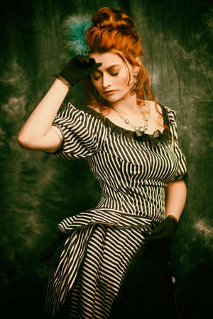 Fashion history, makeup and hairstyle. Portrait of a beautiful red-haired woman in a 19th century dress on a vintage background. Victorian style.の写真素材
