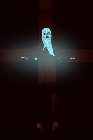 Portrait of scary devilish nun in a dark room in light in the form of a cross. Horrors and Halloween.の写真素材