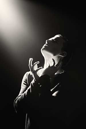 Sensual handsome man posing facing the beam of light coming from above. Art black-and-white...