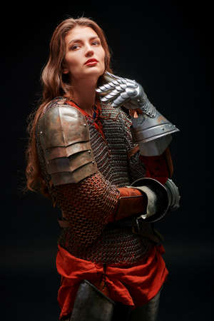 Portrait of beautiful dreamy medieval girl warrior in chainmail and plate armor posing on a dark background.の写真素材