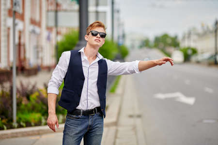 Handsome young man looks for a taxi in street of the city. Summer fashion. Summer holidays and vacation.の写真素材