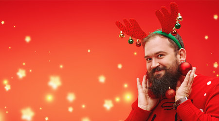 Portrait of a funny hipster man with a beard decorated with Christmas balls smiling at camera.Modern...