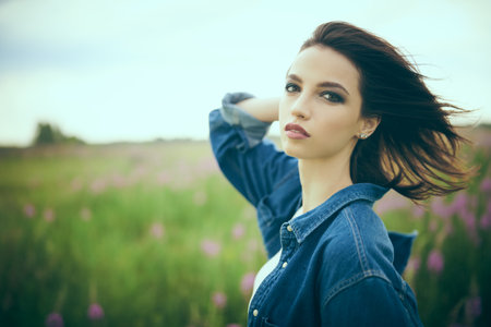 Portrait of a beautiful brunette girl in denim clothes standing in a valley against cloudy sky. Beauty, fashion. Denim style.の写真素材