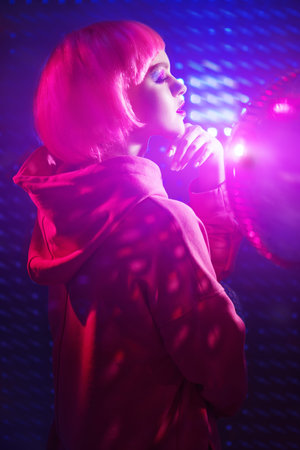 Portrait a modern girl with bright glitter make-up and pink hair posing in the neon lights of the...