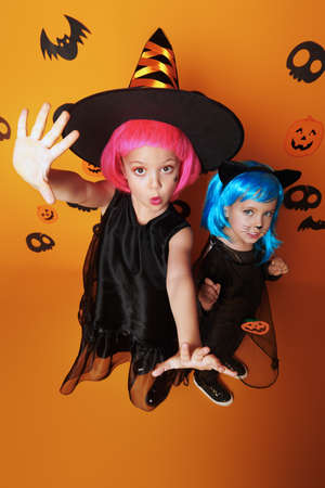 Two cute girls children in carnival costumes posing together on a yellow background. Halloween for kids.の写真素材