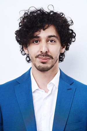 Portrait of a happy young man with dark curly hair and in classic blue suit and a white shirt...