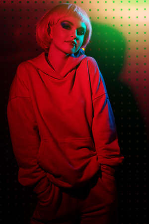 Modern girl with bright makeup and pink hair poses in red light on a background in techno style. Sport chic fashion. Youth fashion and beauty trends.の写真素材