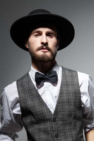 Portrait of a handsome brunet man in elegant classic suit and a black hat on a gray background. Men's beauty. Fashion.の写真素材