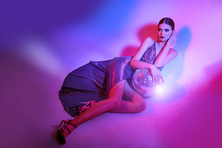 Beautiful professional dancer girl posing in a shiny evening dress with a mirrored disco ball....