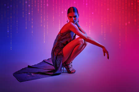 High fashion shot. Beautiful dancer girl poses in a long shiny evening dress and high heels in mixed neon light. Ballet show.の写真素材