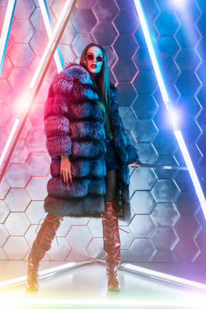 Modern fur coat fashion. Full length portrait of a stunning fashion model girl in expensive silver fox fur coat posing among the neon lamps. Futurism, techno style.の写真素材