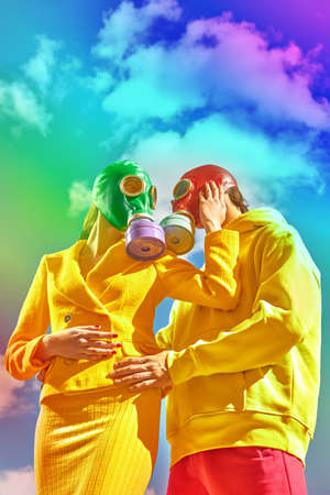 Air pollution, environmental disaster. A loving man and a woman touch each other tenderly against the background of a clear sky with white clouds. They wear bright clothes and gas masks.の写真素材