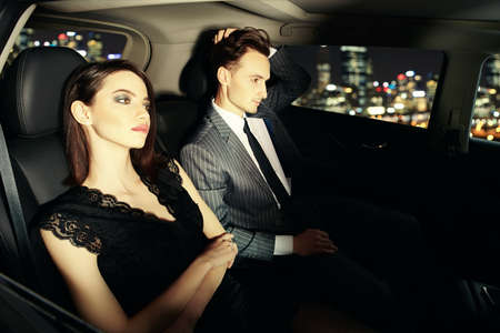 Stylish couple of young people in evening dresses driving through the city at night. Glamorous lifestyle, night party. Evening fashion.の写真素材