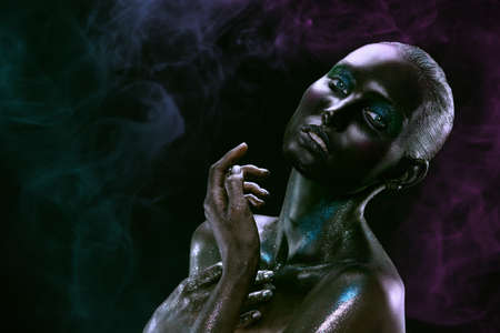 Body painting and makeup. Portrait of a beautiful fashion model girl with sparkling glitter makeup. Black background with a smoke. Copy space.の写真素材