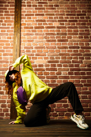 Hip-hop dancer. Cool street dancer girl in bright trendy clothes and sunglasses dancing by a brick...