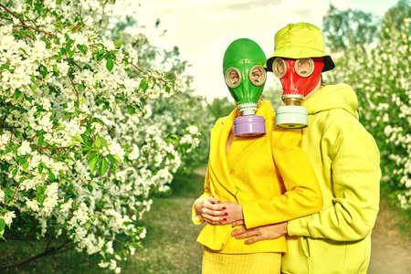 Air pollution, environmental disaster. A loving man stands close to his beloved girl in a blossoming apple orchard. They wear bright clothes and gas masks. Modern art.の写真素材