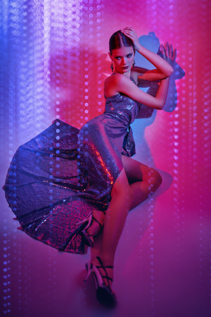 High fashion shot. Beautiful dancer girl poses in a long shiny evening dress and high heels in mixed neon light. Ballet show.の写真素材