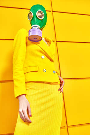Fashion of the future. Full length portrait of a woman in elegant yellow suit and green gas mask posing by a yellow industrial wall. Environmental disaster, apocalypse.の写真素材