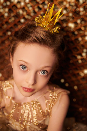 Close-up portrait of a beautiful little princess girl in a golden dress and a crown in her vintage castle. Fairy tales.の写真素材