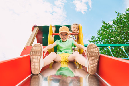 Happy childhood. Summer holidays. Cheerful children ride a slide on a playground in the park.