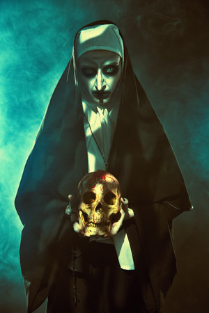 Devilish evil nun stands in a mystical fog with a skull in her hands. Halloween and Horrors.の写真素材