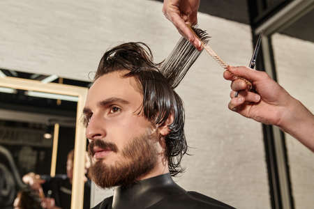 Barbershop. Good looking brunet man getting haircut by hairdresser while sitting in a chair at barbershop.の写真素材