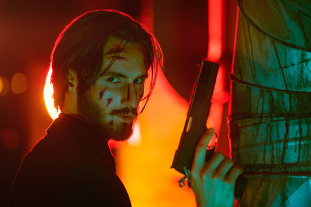 Portrait of a handsome wounded special agent standing on alert with a gun in his hand in backstreet of the night city.の写真素材