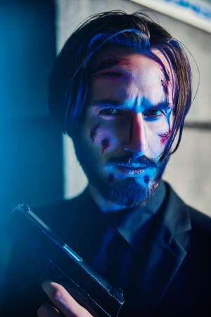 Close-up portrait of a wounded action hero man with a gun in his hand in the light of the night city.の写真素材