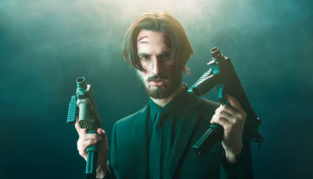 Brave special agent in a black suit with automatic guns in his hands on a dark foggy background.の写真素材